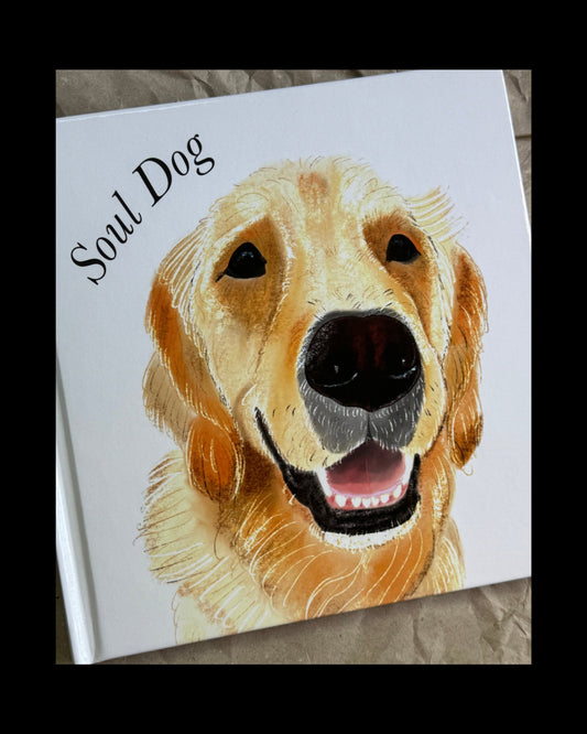 A square white hardcover book titled 'Soul Dog' featuring a painted golden retriever on the cover, photographed on a crumpled brown paper background.