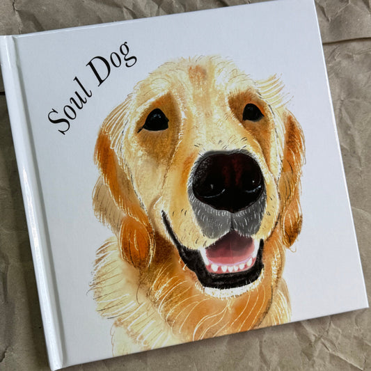 A square white hardcover book titled 'Soul Dog' featuring a painted golden retriever on the cover, photographed on a crumpled brown paper background.